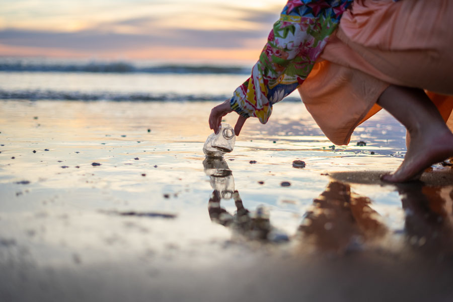 Environmental Insurance - Woman Picking Up Bottle at the Beach